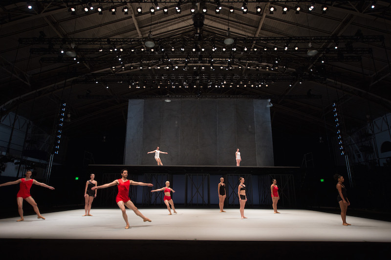 Dancers in black, white and red unitards perform on the first and above stages. 
